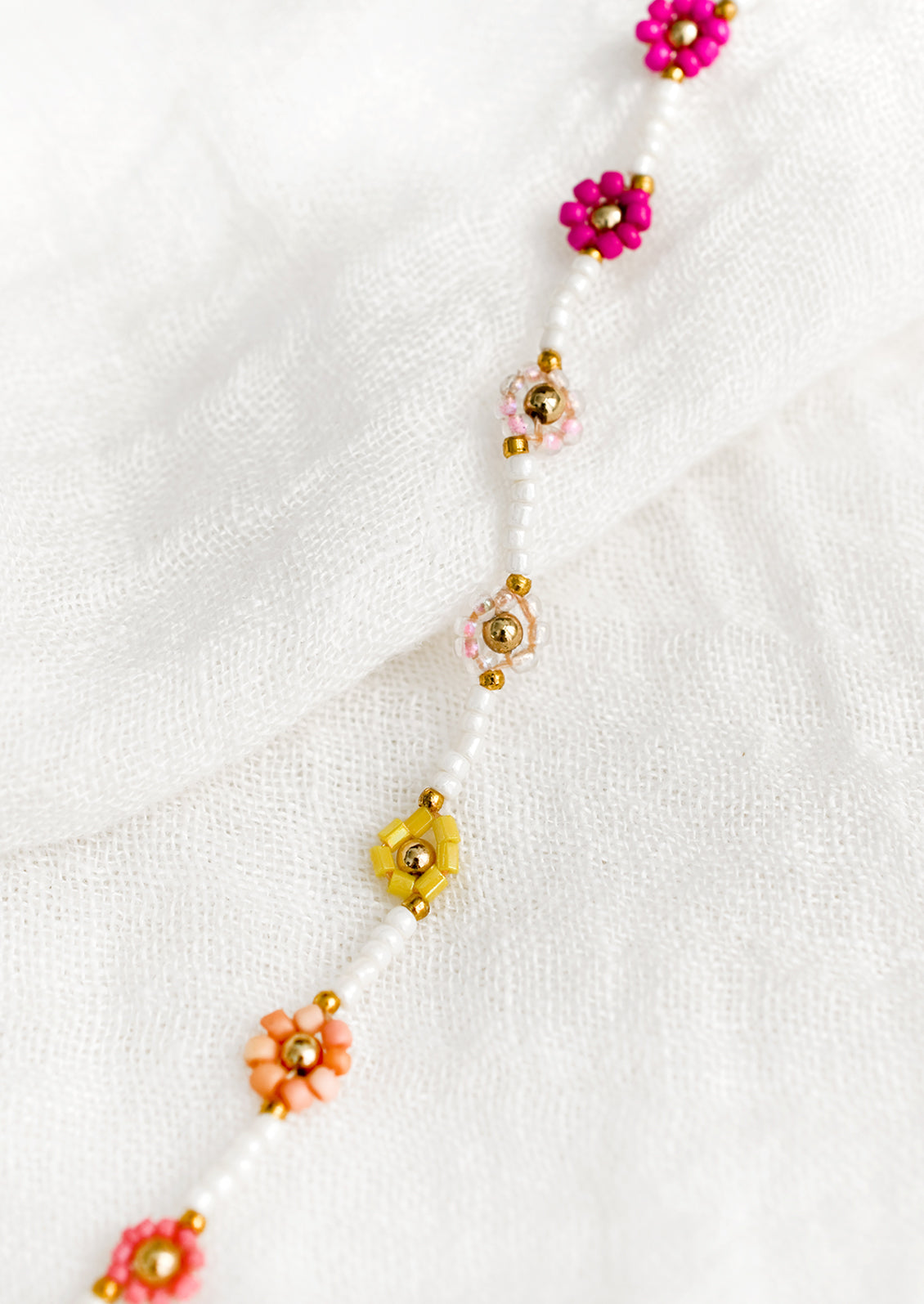 A white beaded bracelet with pink and yellow beaded flowers.