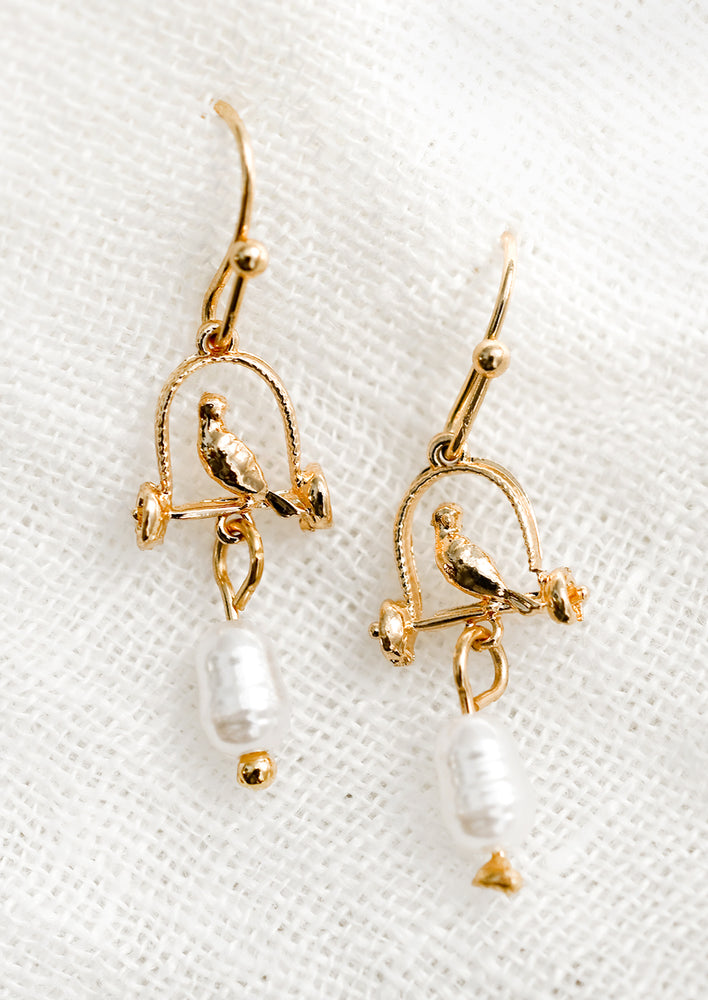1: A pair of gold earrings depicting bird sitting on perch, with pearl bead.