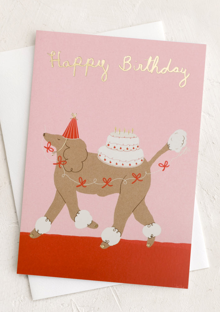 A card with image of a poodle carrying a birthday cake, text reads "Happy Birthday".