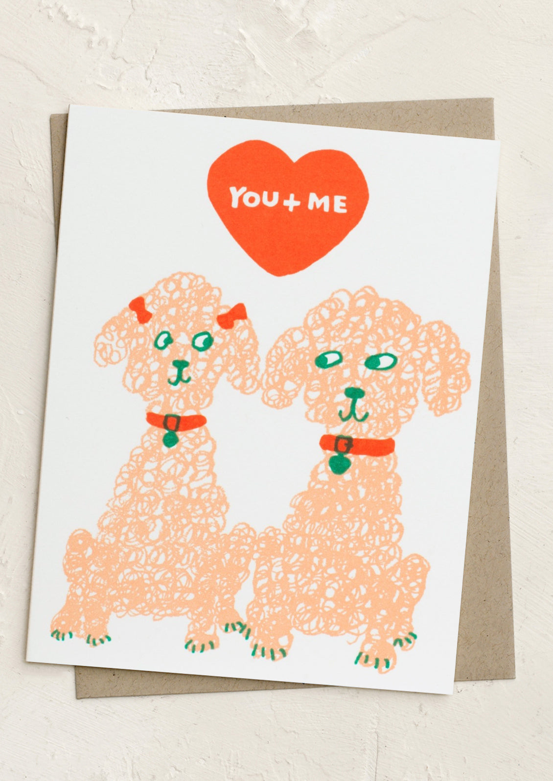 A card with sketch of two poodles, red heart and top with text reading "You + me".