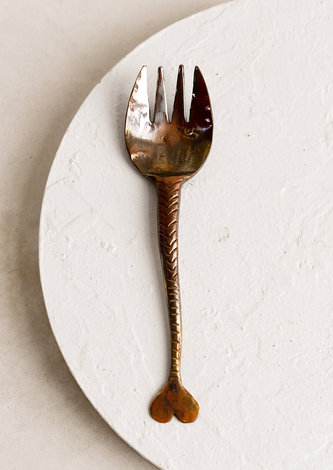 A copper fork with fish tail handle and oxidized finish.