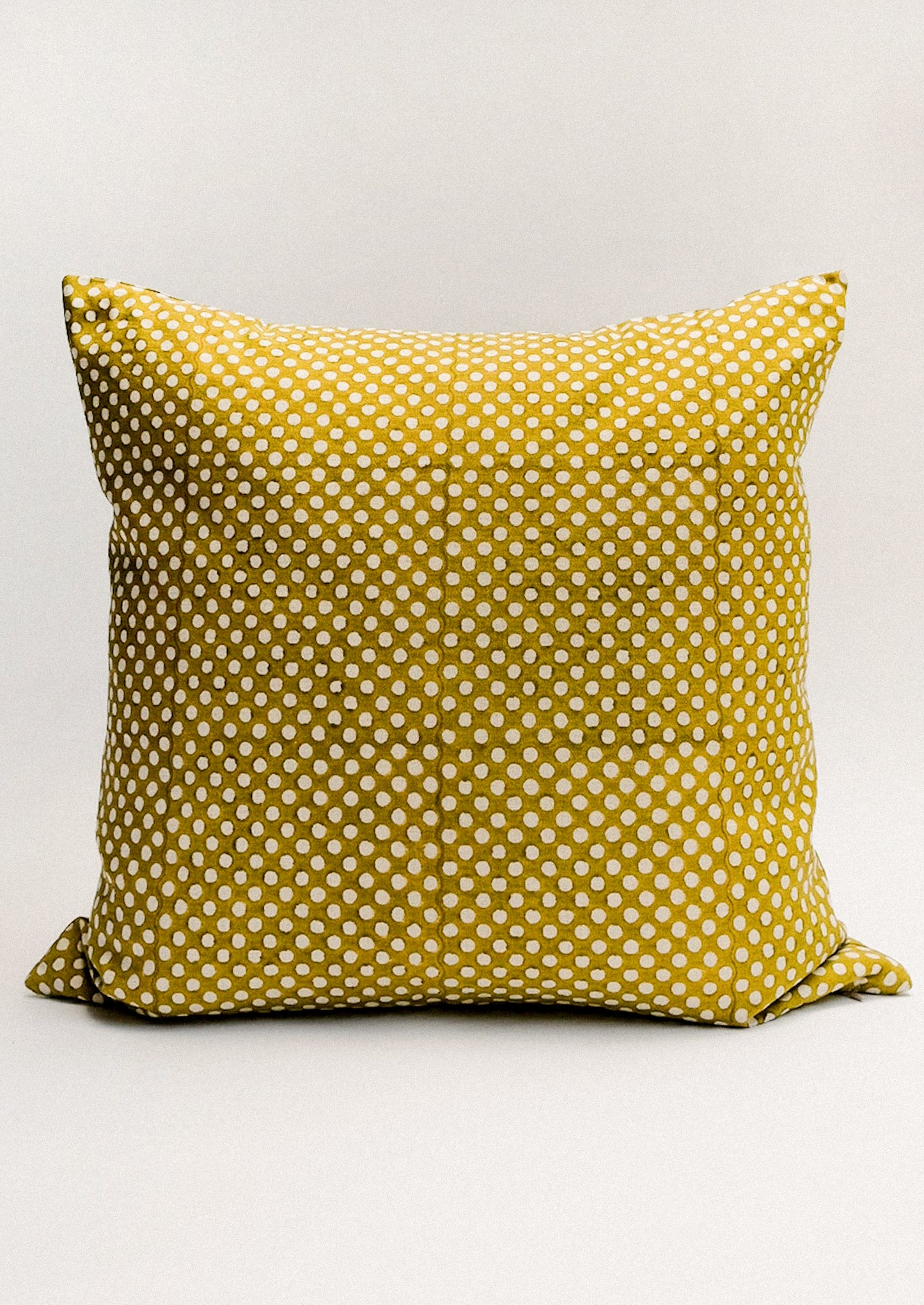 A chartreuse throw pillow with contrast polka dot pattern.