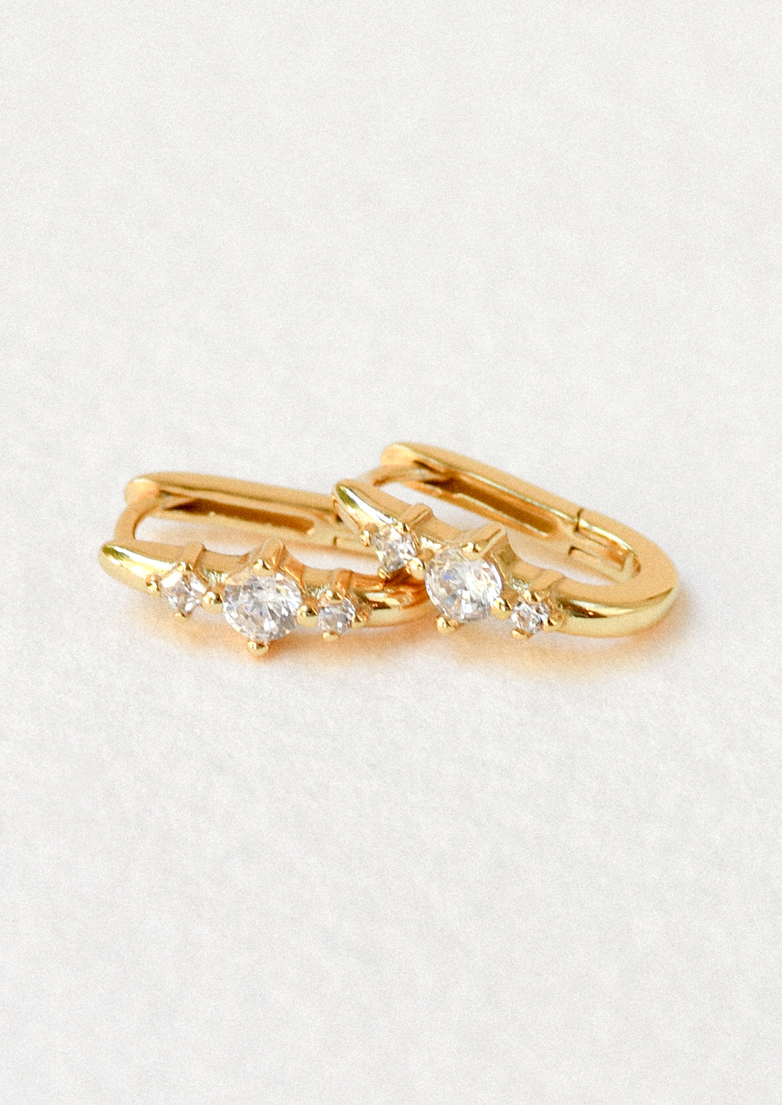 A pair of gold huggie hoop earrings with a trio of pronged cubic zironia gems.