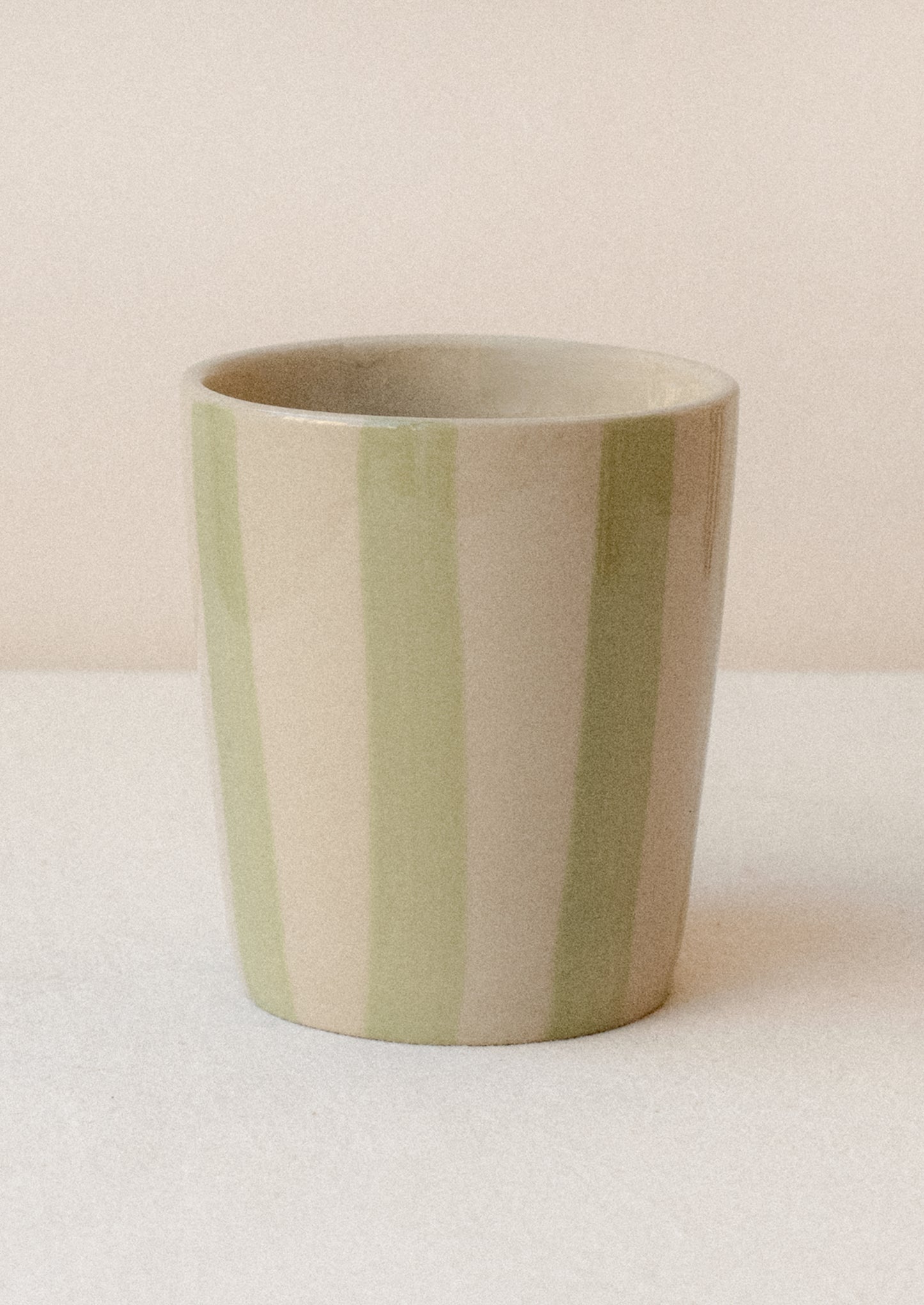 A striped ceramic cup in bisque with light green vertical stripes.