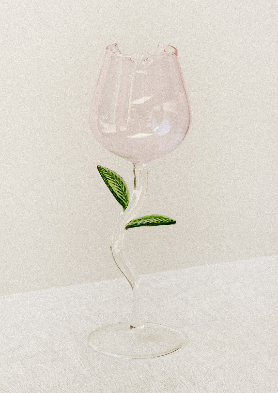 A wine glass in the shape of a pink rosebud, with green leaf detail on stem.