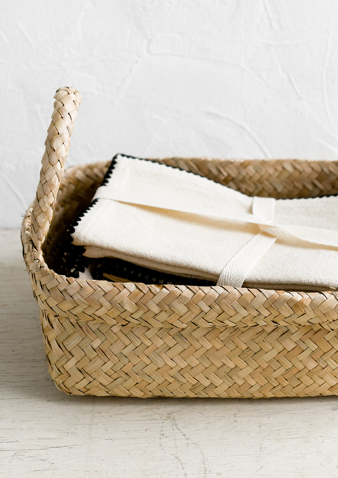 A rectangular seagrass basket with rolled top rim and side handles.