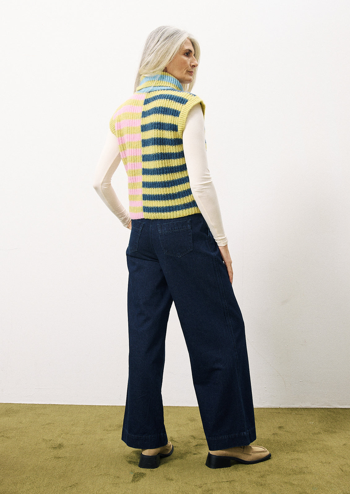 A woman wearing a lime green, navy and pink stripe sleeveless sweater vest with turtleneck.