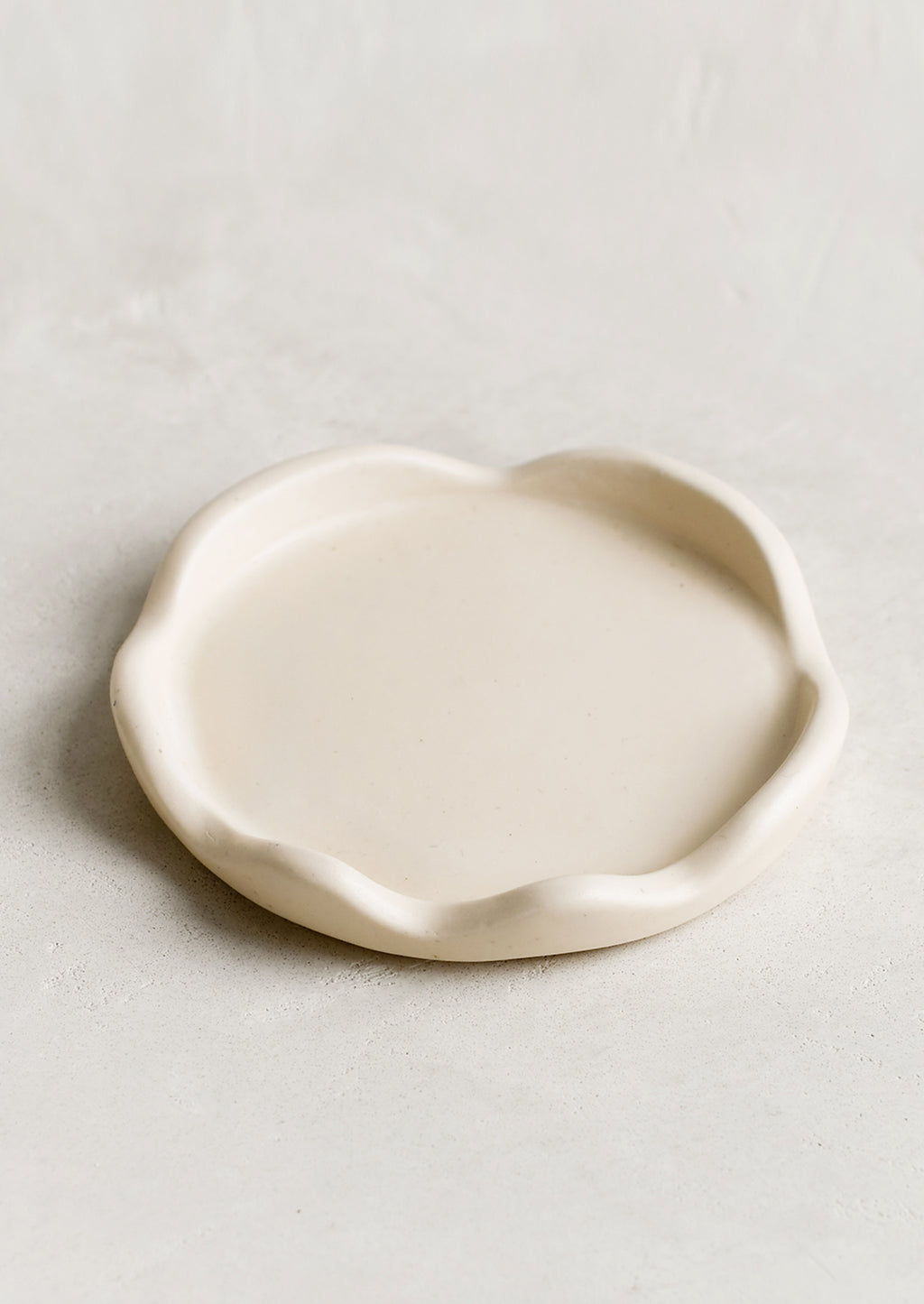 1: A cream resin coaster with curvy scalloped edges.