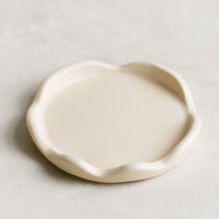 1: A cream resin coaster with curvy scalloped edges.