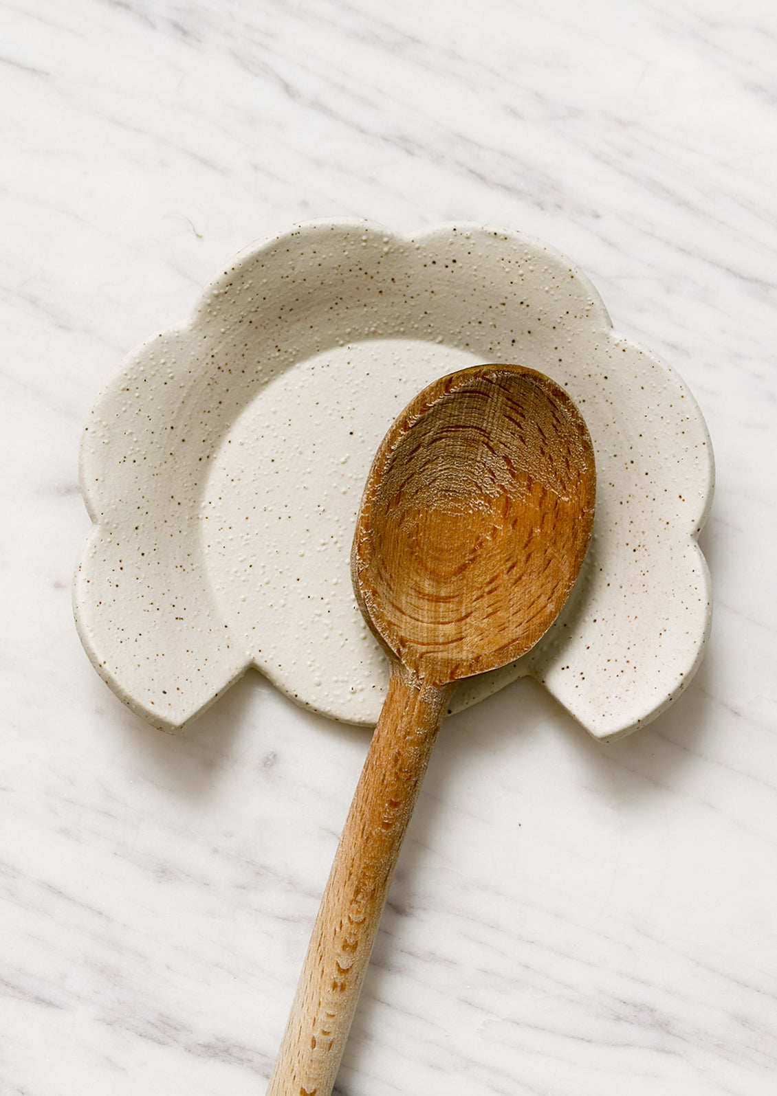 An off-white speckled ceramic spoon rest in half flower shape.