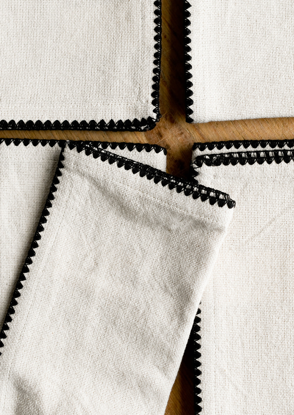 1: A stack of natural cotton dinner napkins with scalloped black stitching.