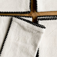 1: A stack of natural cotton dinner napkins with scalloped black stitching.