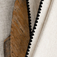 3: A stack of natural cotton dinner napkins with scalloped black stitching.