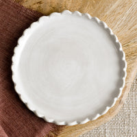 White: A round ceramic plate in white with scalloped edges.