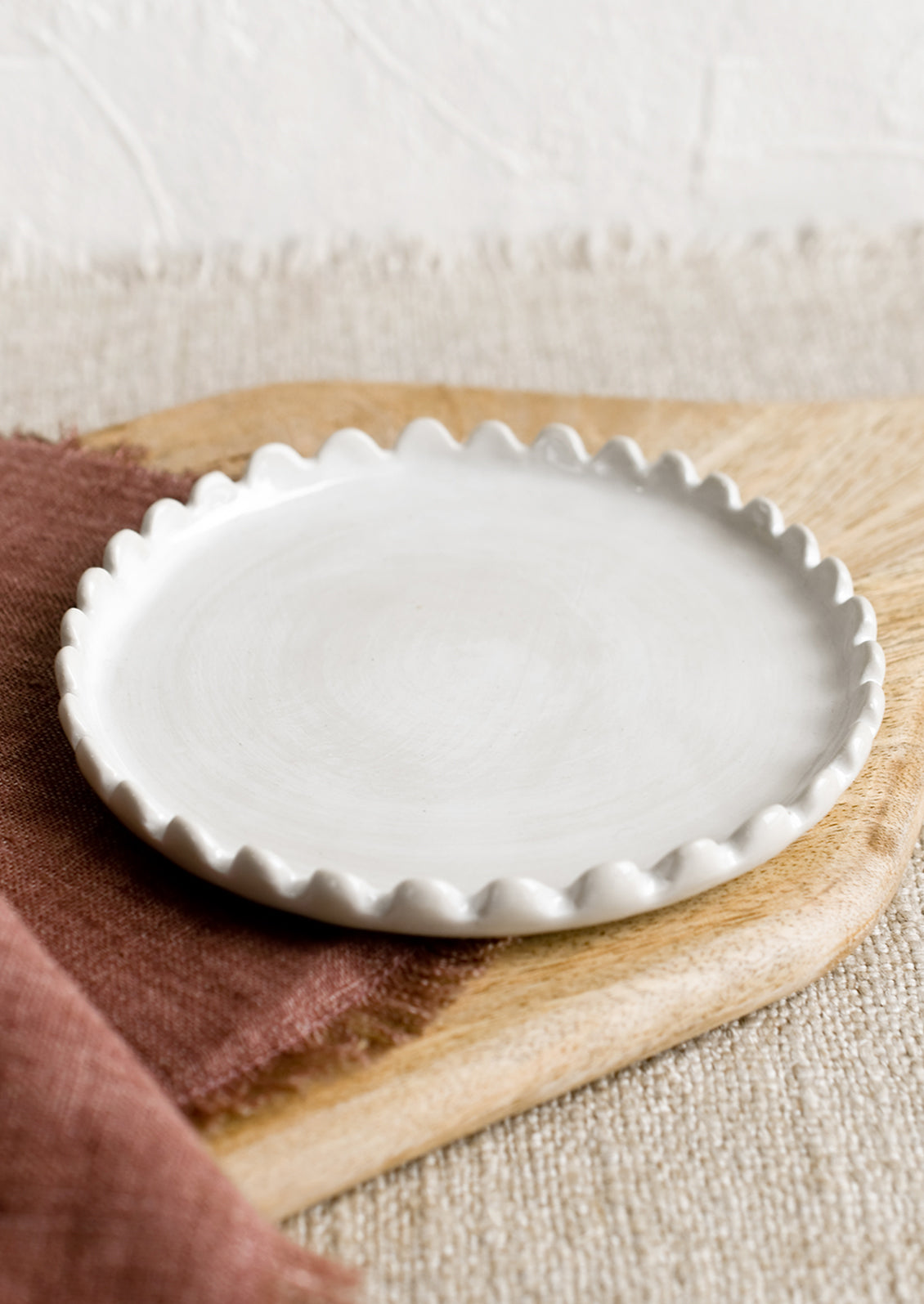 A round ceramic plate in white with scalloped edges.