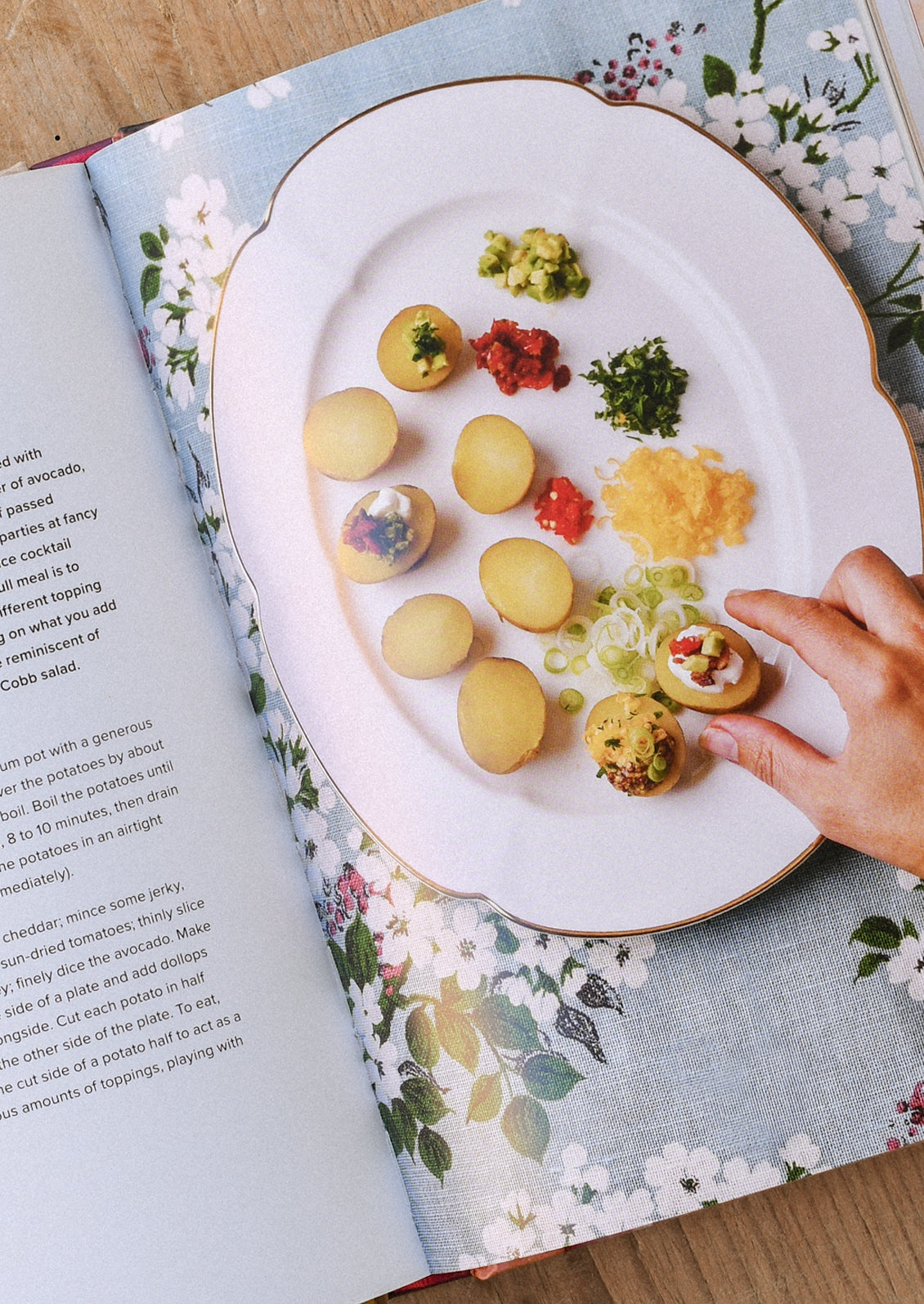 A book open on a table showing a plate with potato bites and a hand grabbing one of the bites.