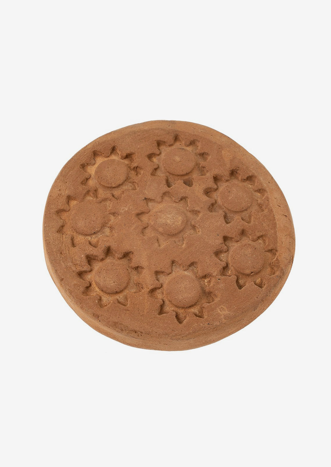 A round terracotta coaster with stamped sun pattern.