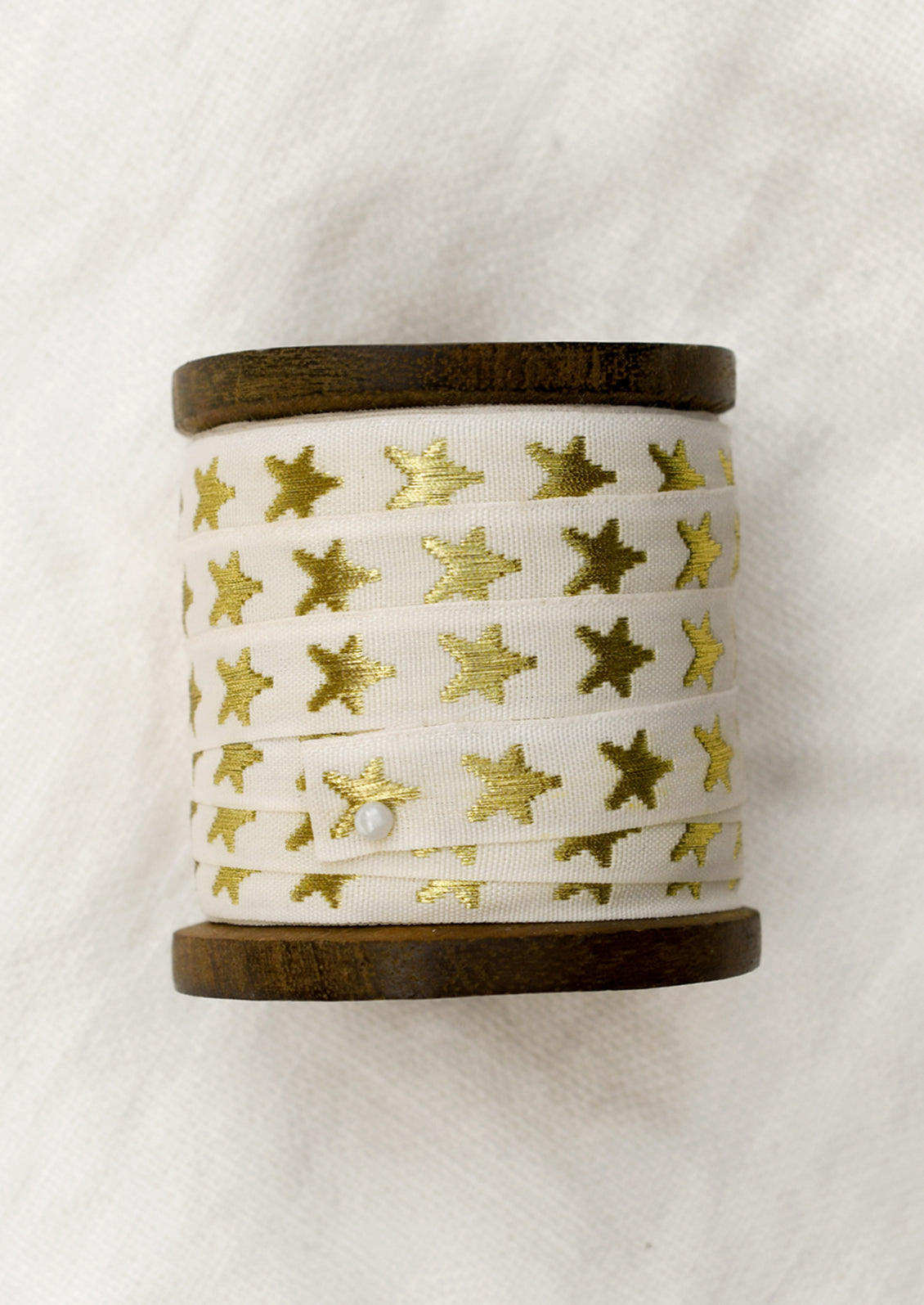 A walnut wood spool with cream ribbon with gold embroidered star pattern.