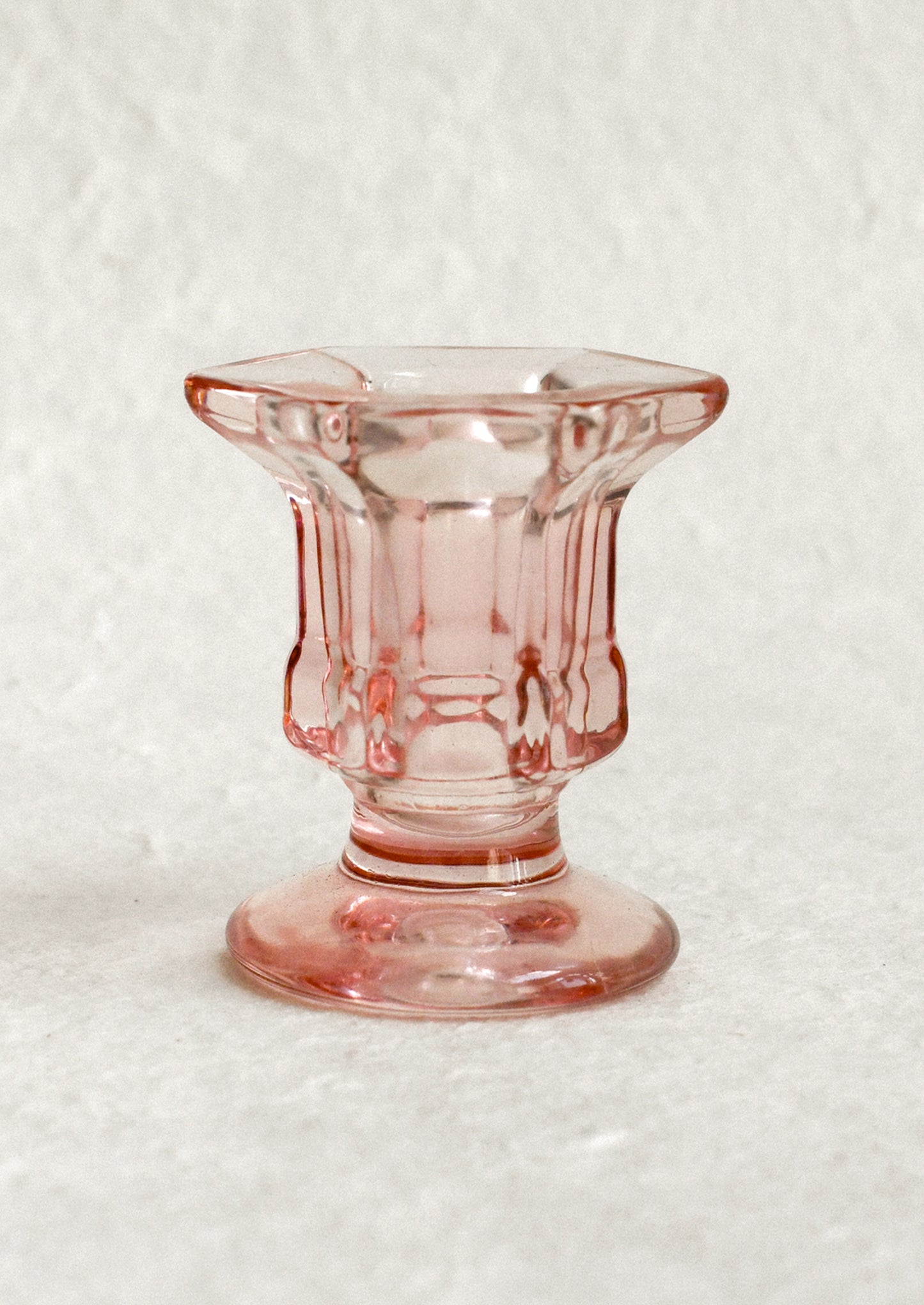 A footed glass candleholder in pink glass.