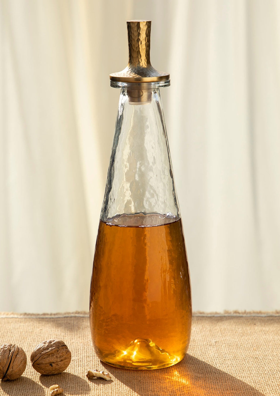 A hammered glass decanter with modern, tapered shape and brass lid.