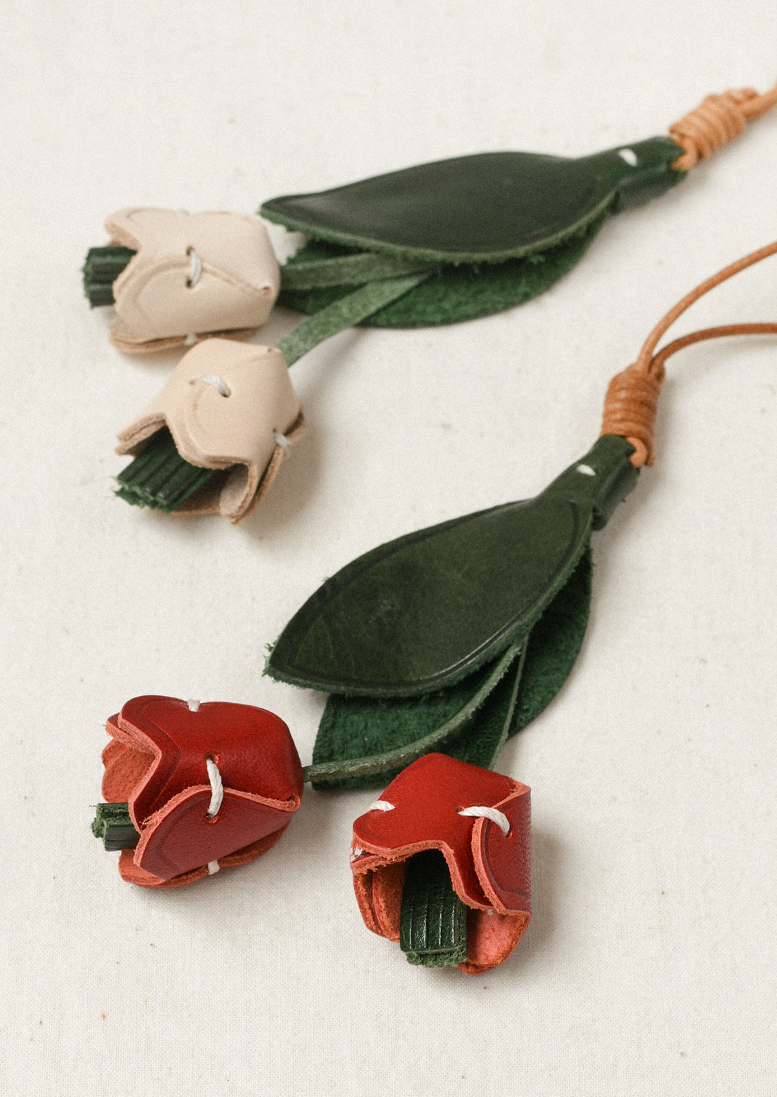 Two leather bag charms shaped like a tulip with red and cream petals and green leaves.