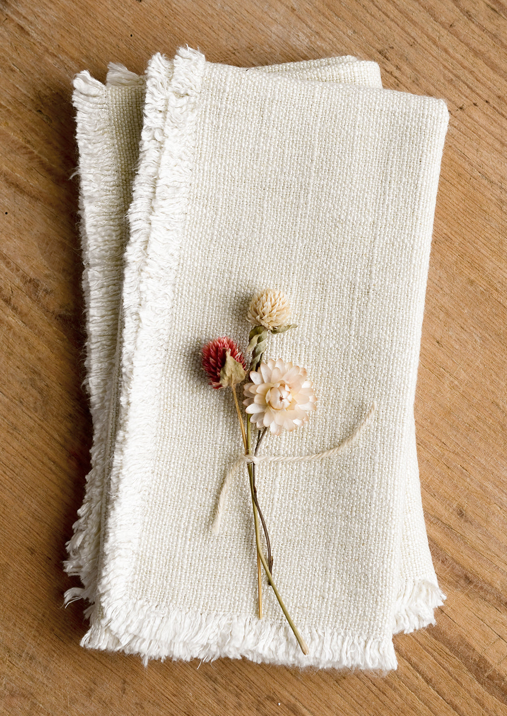 1: A pair of cream linen napkins with linen texture and fringed edges.