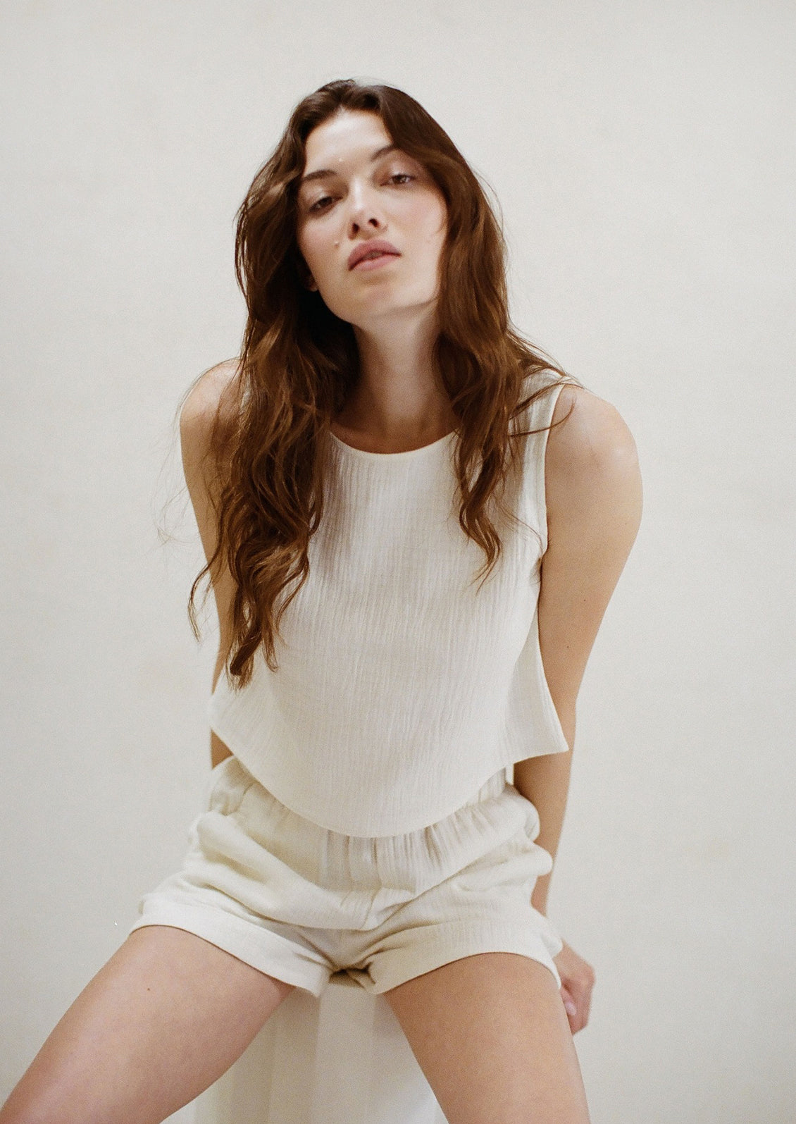 A woman sitting wearing a white cotton gauze tank top and matching shorts