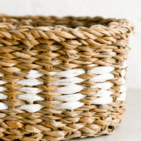 3: An oval shaped storage basket in seagrass with woven white detail.