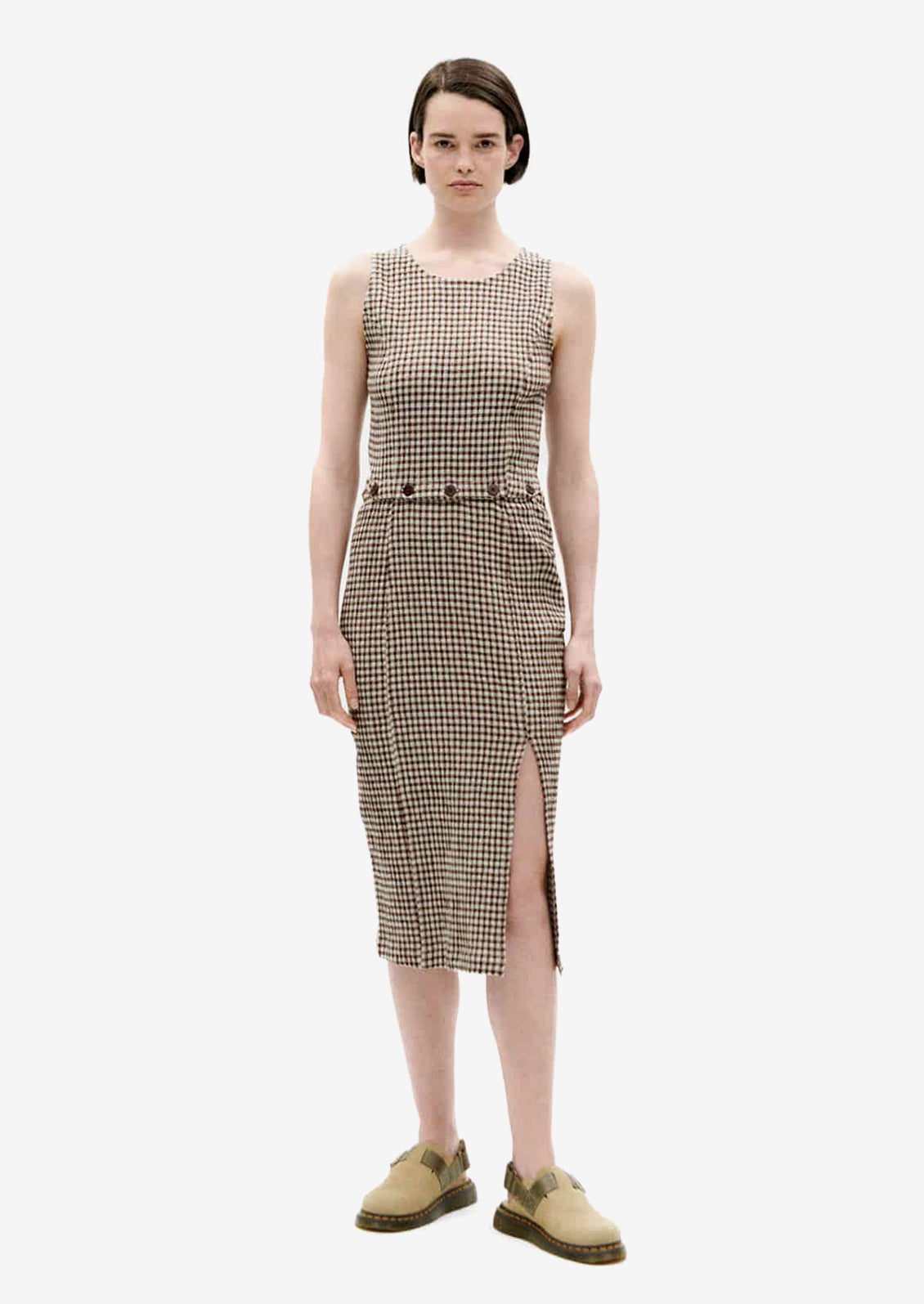 A woman wearing a sleeveless shift dress with button waist detail.