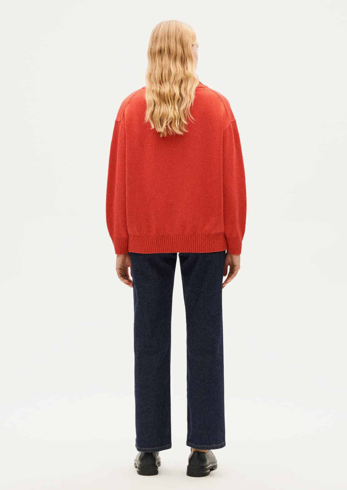 A woman wearing a button front, long sleeve cardigan sweater in red-orange huge.