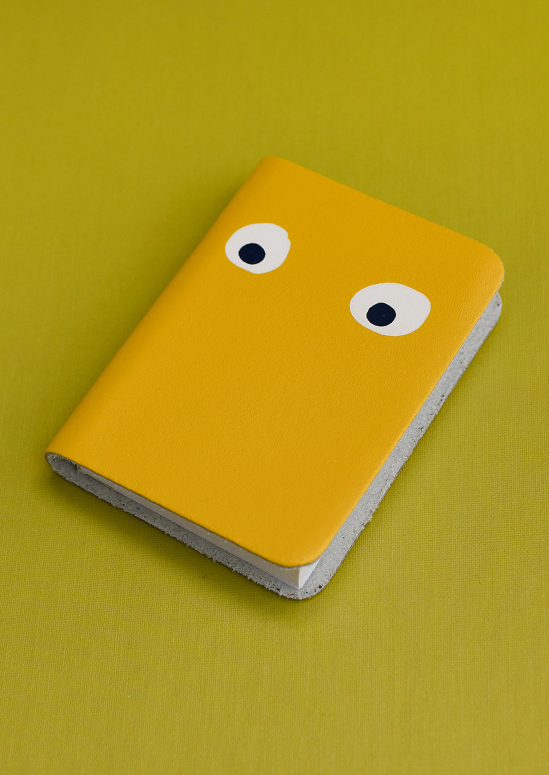 A yellow leather notebook with pair of eyes painted on cover.