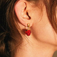2: A person wearing a pair of glass earrings in shape of raspberries.
