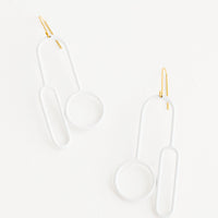 Blanco: Arced white earrings with one circle and one elongated oval at either end on a brass ear wire. 