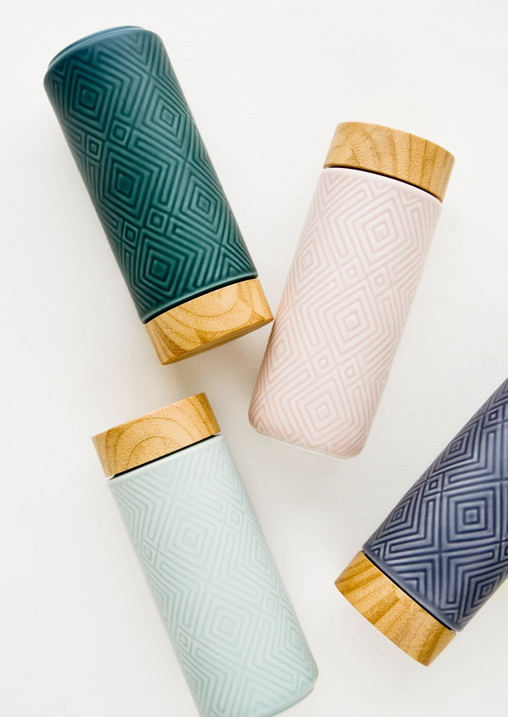 1: A scattered grouping of tall ceramic travel tumblers with tonal geometric patterns