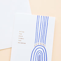 1: White greeting card with cobalt blue rainbow and gold text reading "After the rain comes the rainbow"