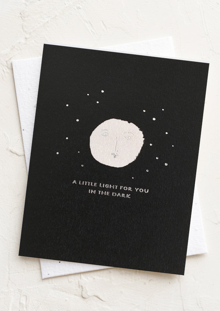 1: Black greeting card with white moon and silver text "A little light for you in the dark"