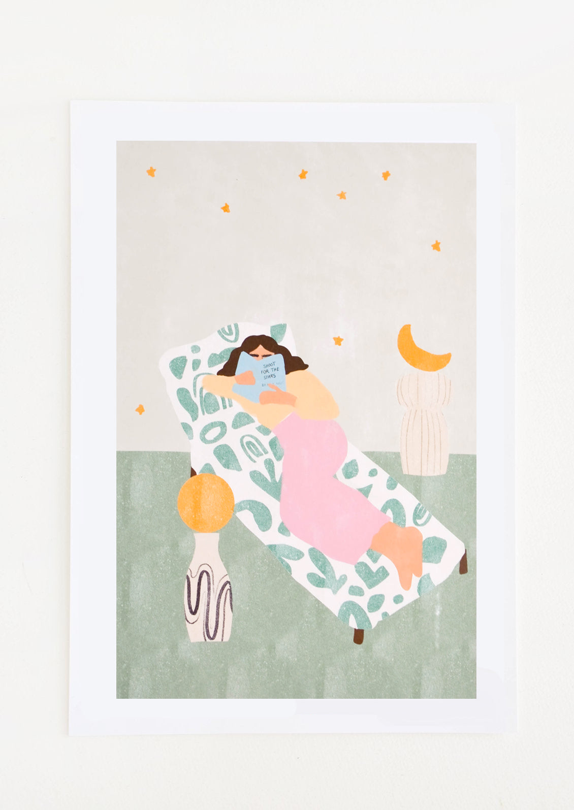 A woman in pink pants reads on a chaise lounge against a gray star filled sky.