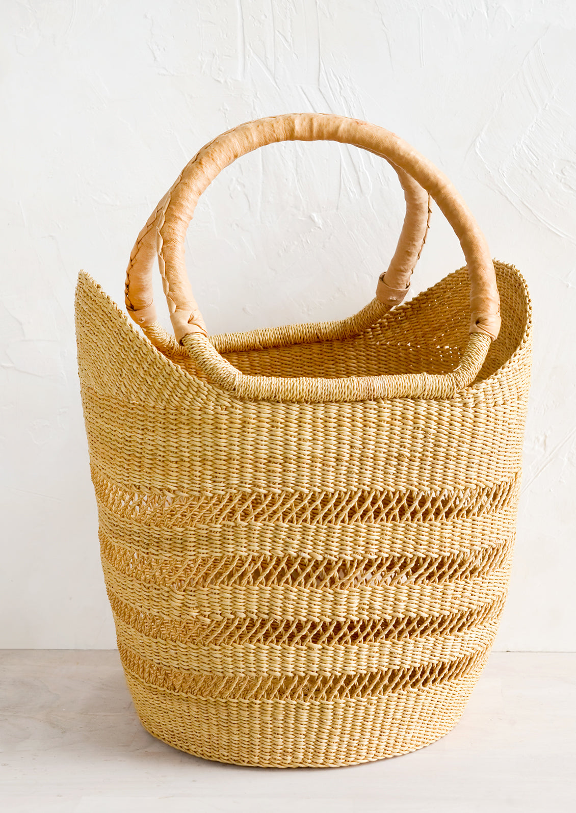 A basket tote woven from natural elephant grass with natural leather wrapped handles.