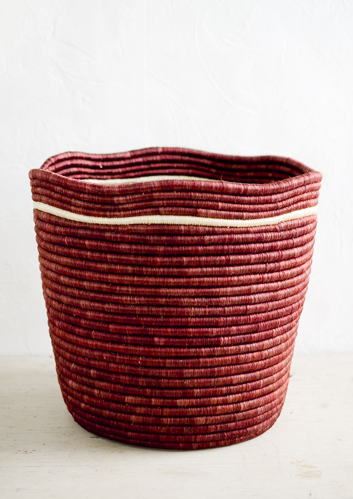 A woven sweetgrass storage bin in merlot color with a wavy top rim and contrast stripe detail around rim.
