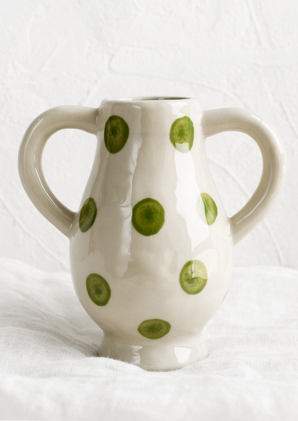 A ceramic vase in green dot pattern with side handle detail.