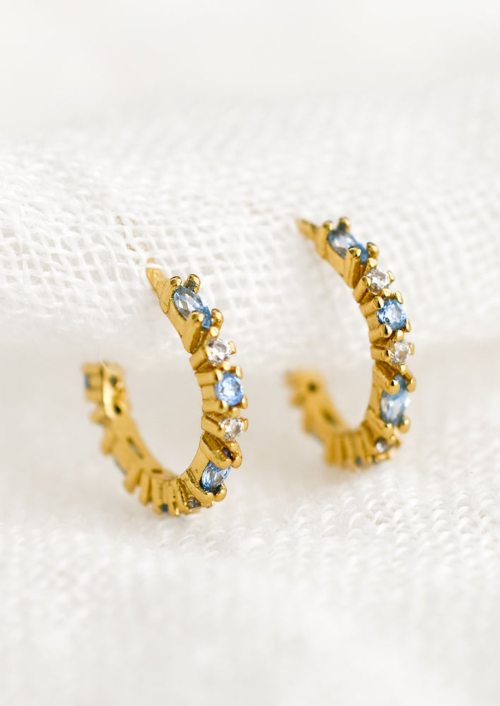 A pair of gold hoop earrings with blue and clear crystals.