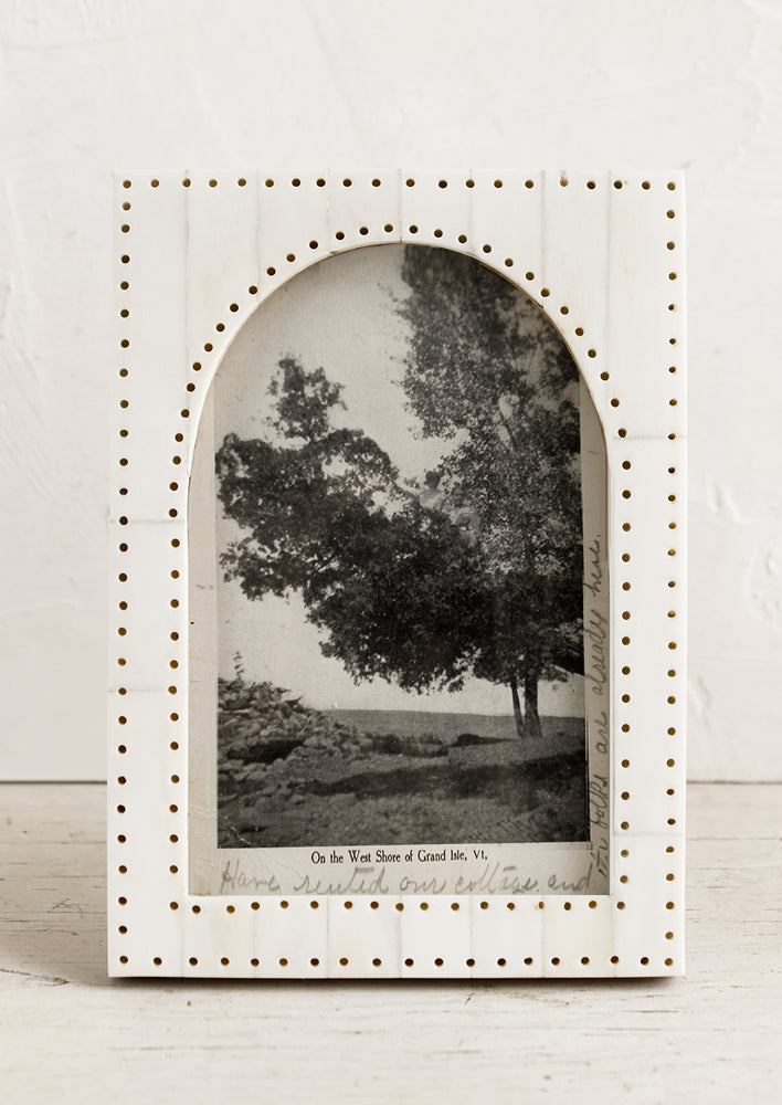 1: An ivory colored picture frame with cutout and perforation detailing in shape of an arch.