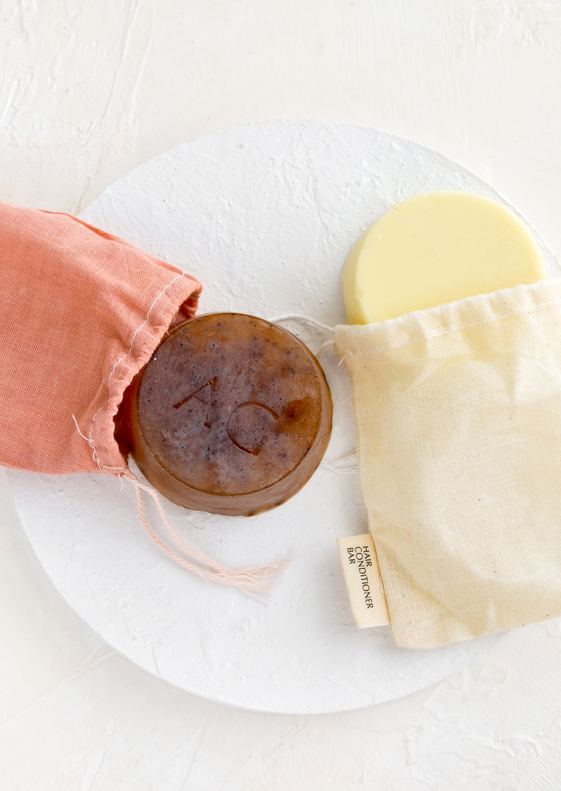 Round solid shampoo & conditioner bars in muslin packaging.