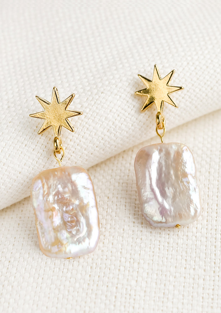 A pair of earrings with gold star shaped post and pink square pearls.