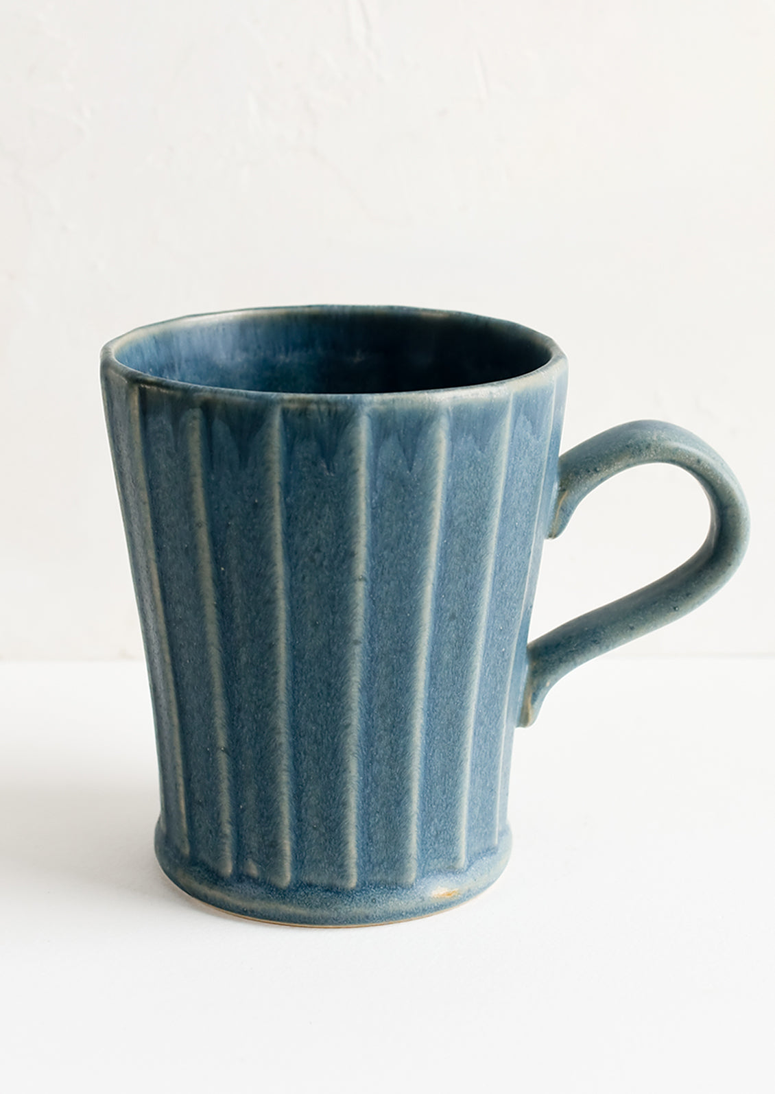 A blue ceramic mug with fluted texture and tapered bottom.