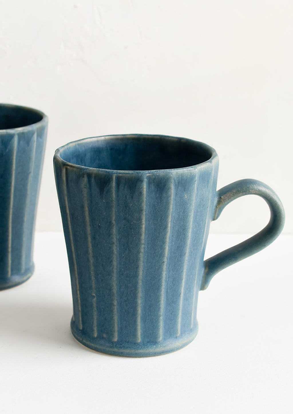 1: Blue ceramic mugs with fluted texture and tapered bottom.