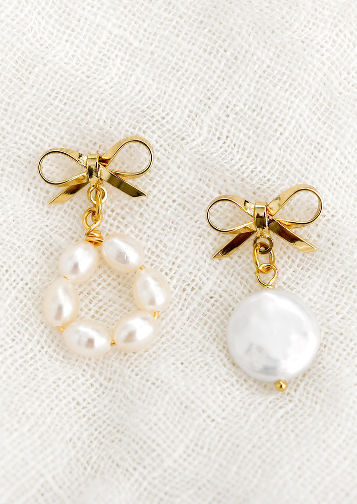 A pair of gold bow earrings with mismatched pearl beading.