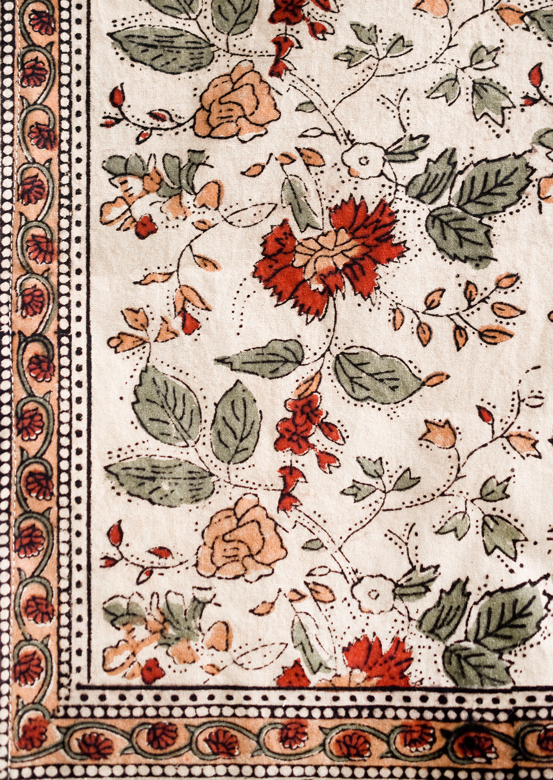 A block printed table runner in crimson, green and beige floral print.