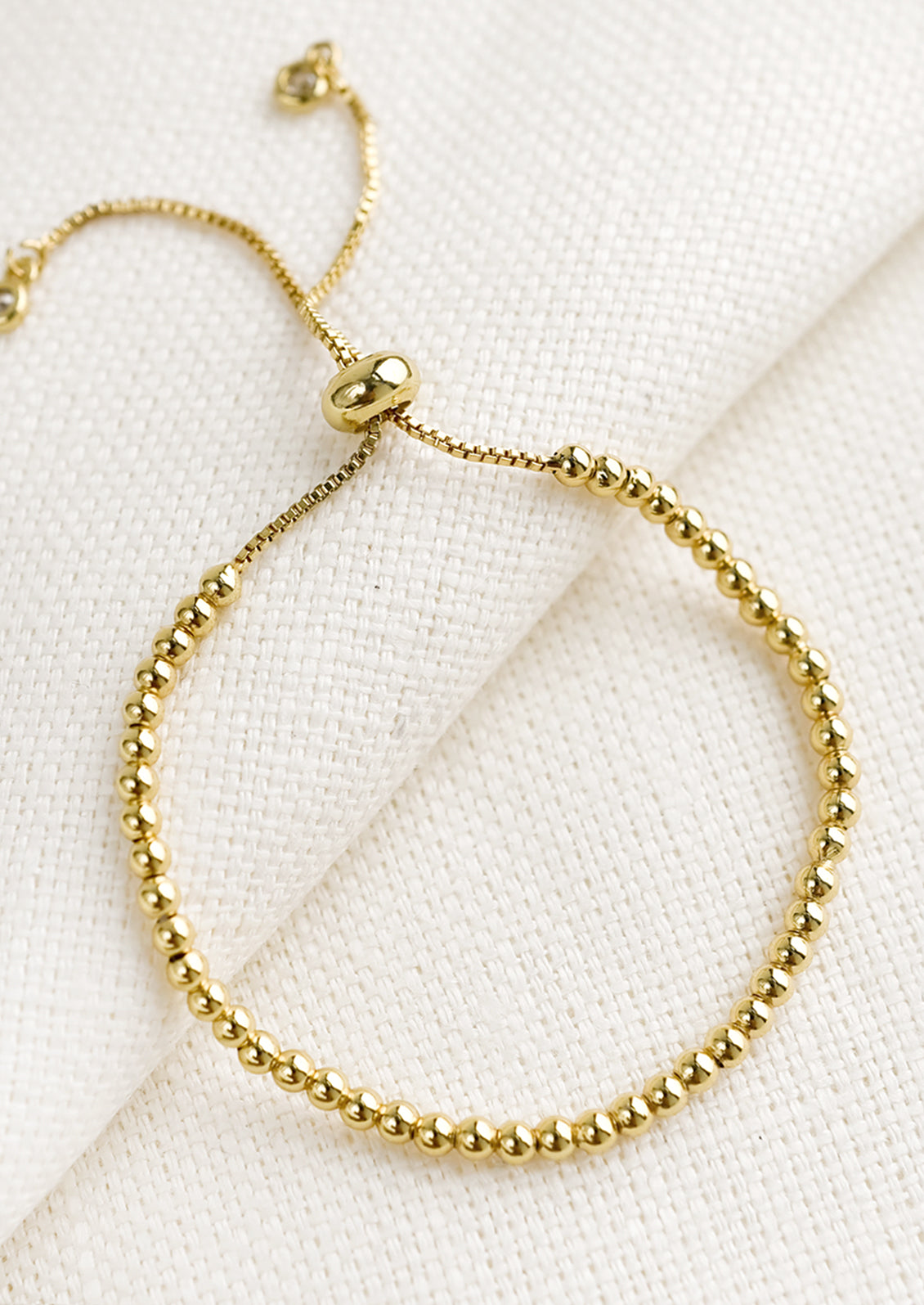 A gold bracelet with sliding closure and ball chain beading.