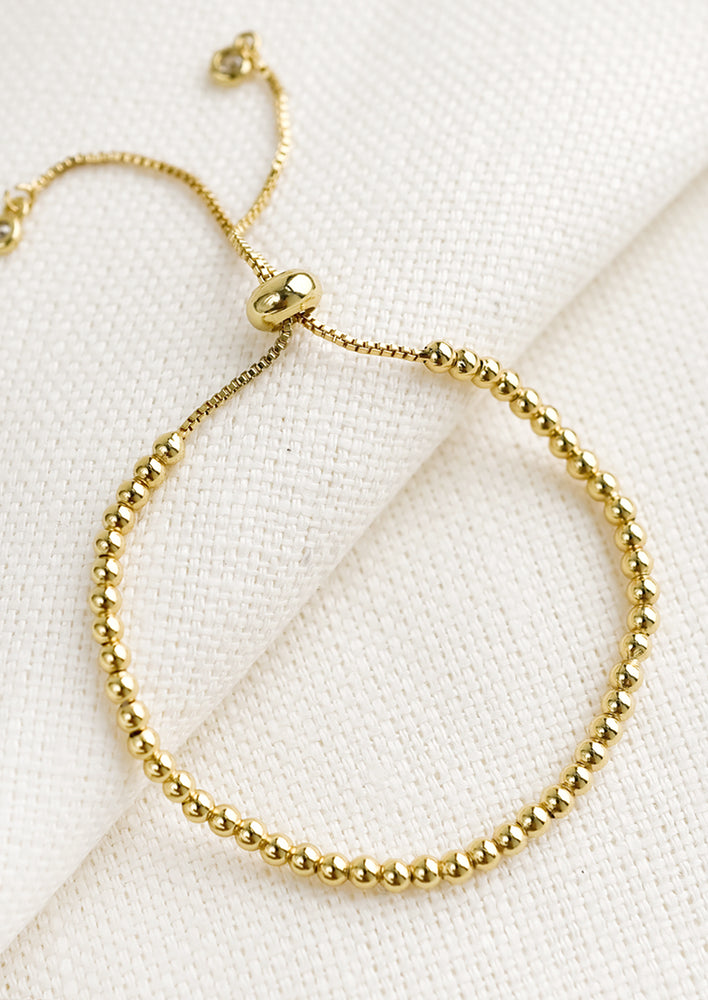 1: A gold bracelet with sliding closure and ball chain beading.
